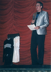 Microphone in hand, Paul stands beside the two hanging costumes.