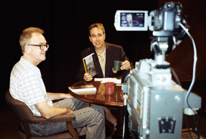 Seated in studio, Paul interviews Tim.